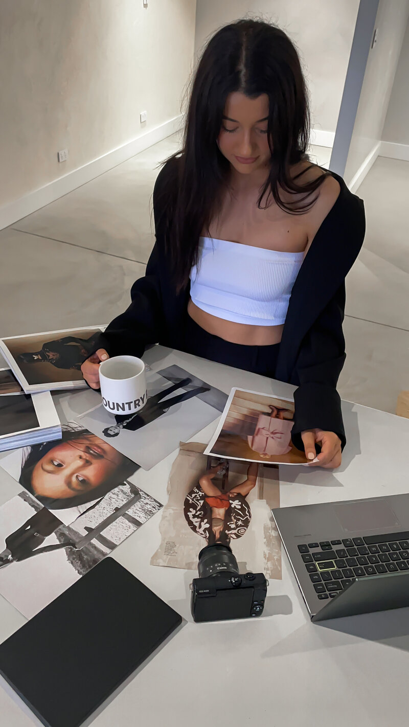 Girl at concrete table holding coffee cup and looking at photos from a magazine