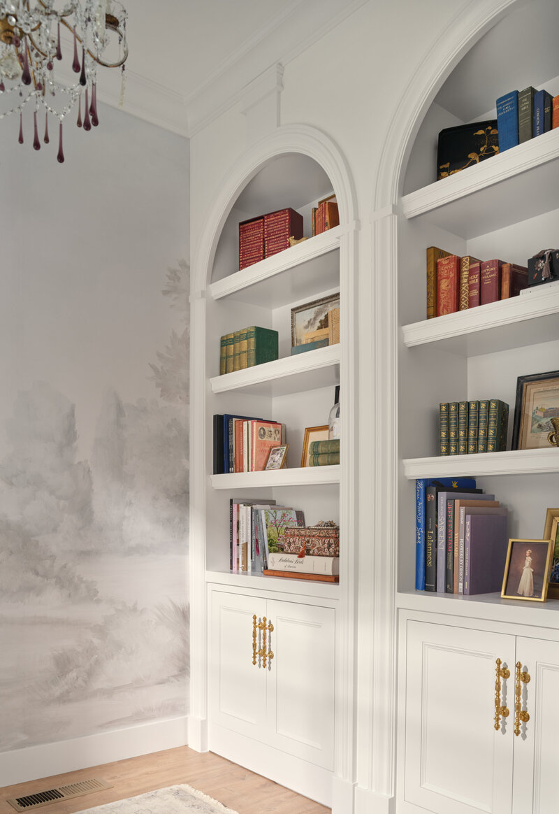 arch built in book shelve with color coded books and gold hardware on cabinets