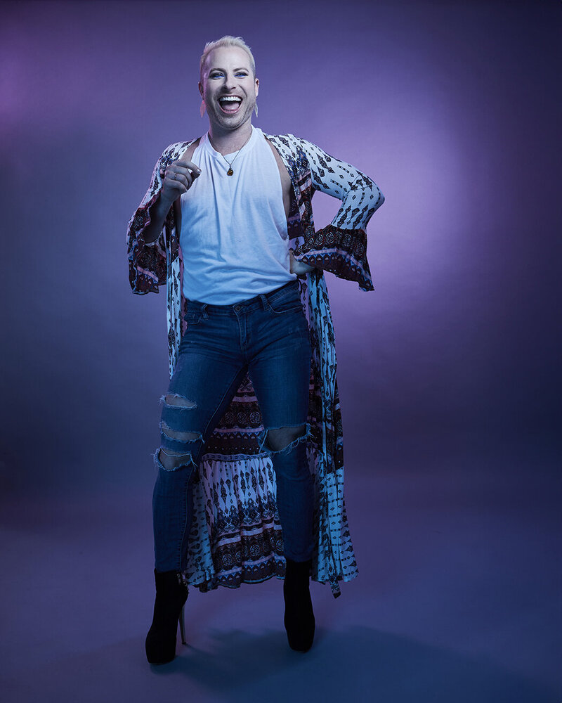 Dynamic full-body shot of Dain August in a shimmering blue outfit, striking a bold pose with dramatic lighting, captured by Ylva Erevall.