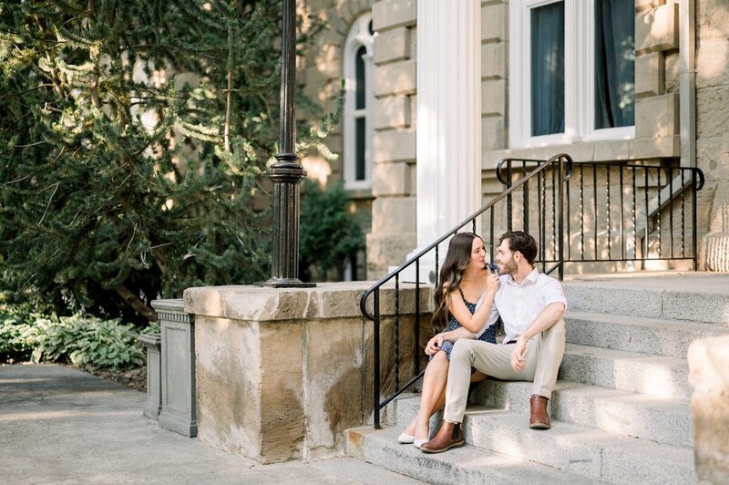 A couple sitting close together on steps outside a building with classic architecture, engaged in intimate conversation.