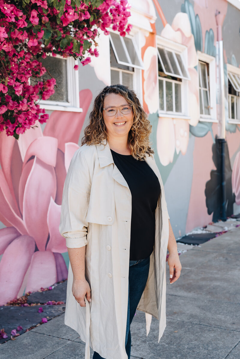 Emily Owner of Woodall Creative Co smiles at the camera with a beautiful pink and white mural behind her.