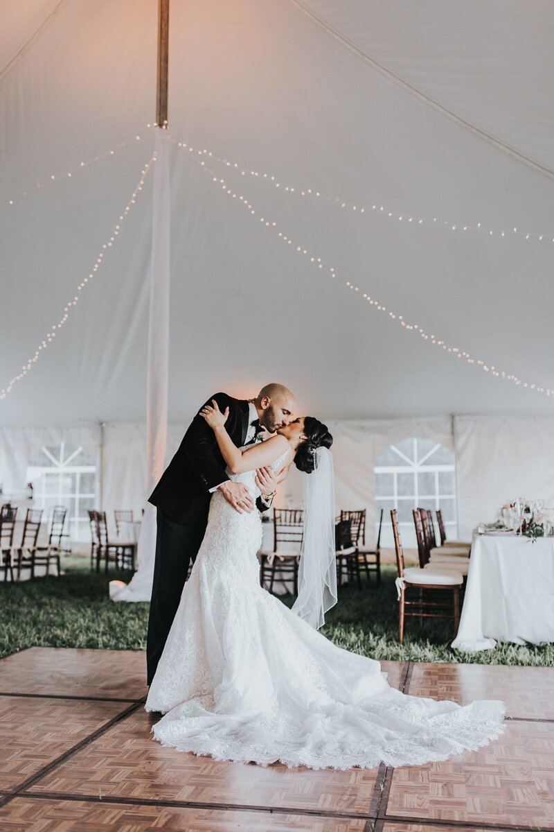 Groom dips bride for kiss at tented wedding reception