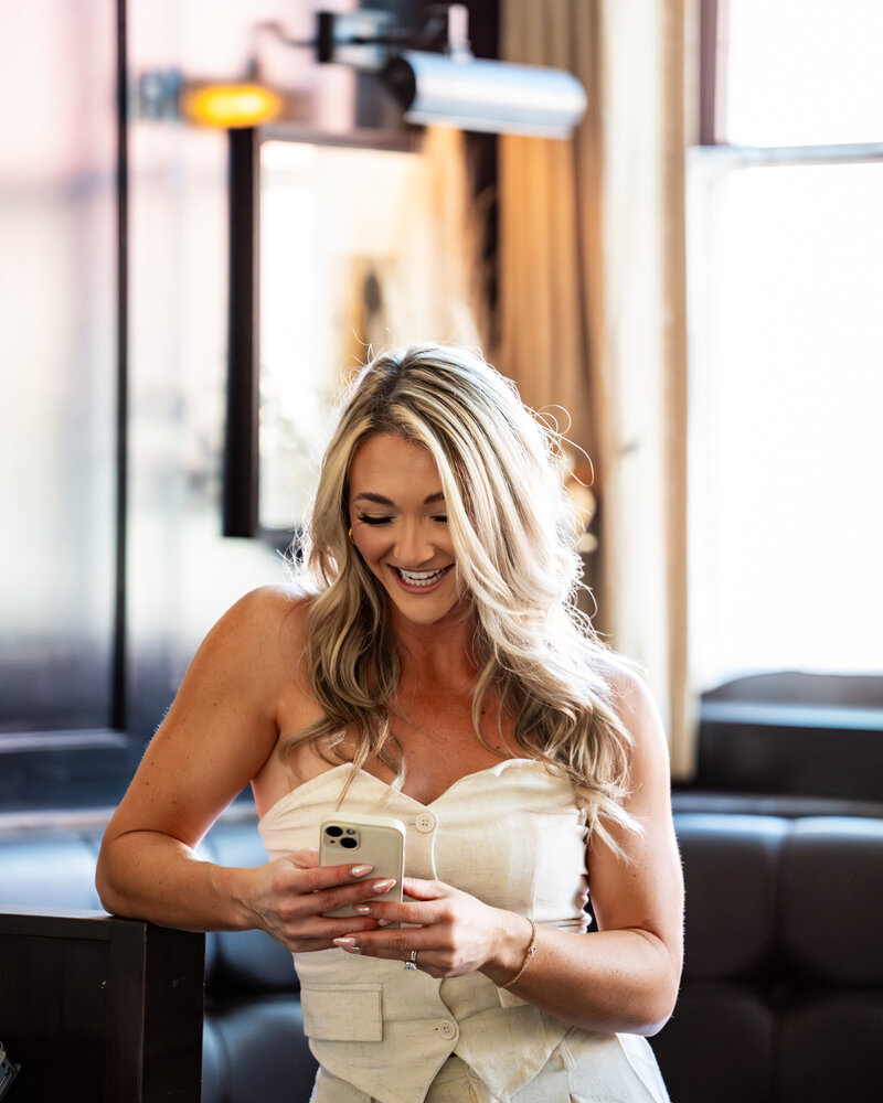 Zoe Schroeder, fitness and nutrition coach, smiling while looking at her phone, supporting clients with personalized coaching and advice.