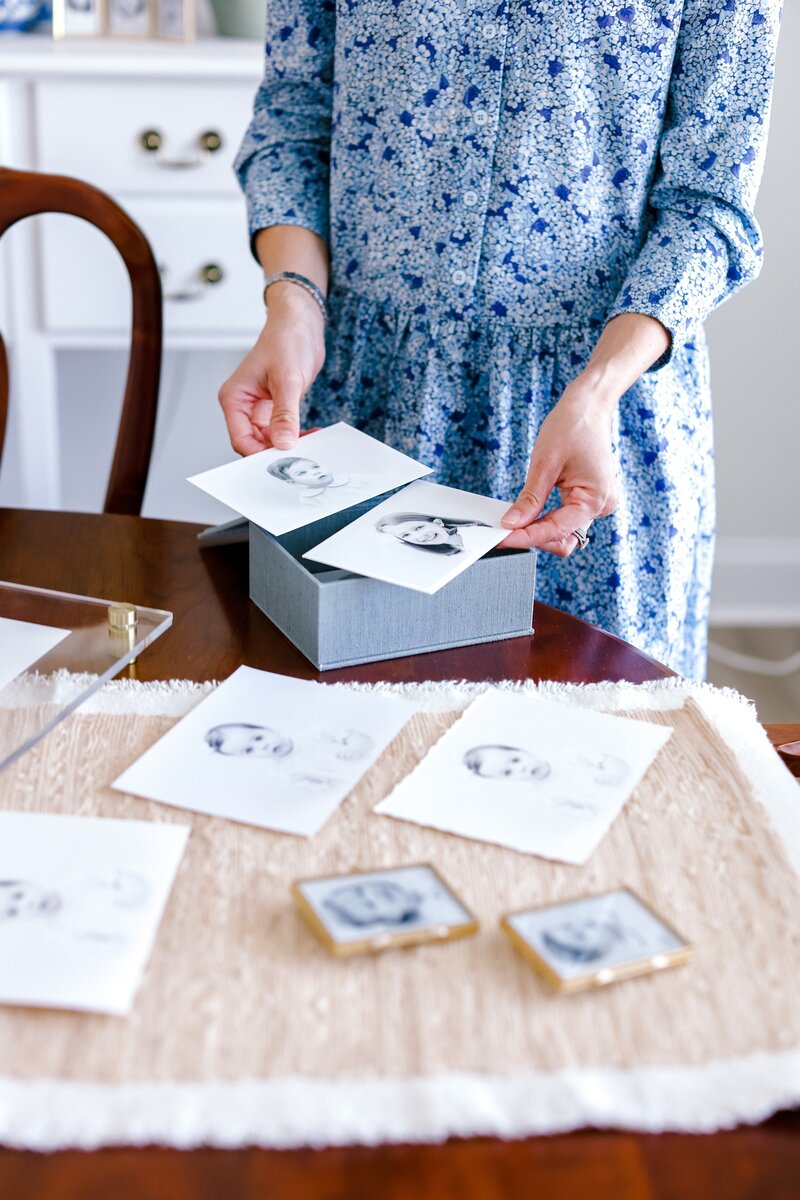 Woman in a blue dress organizing printed black and white portraits on a table.