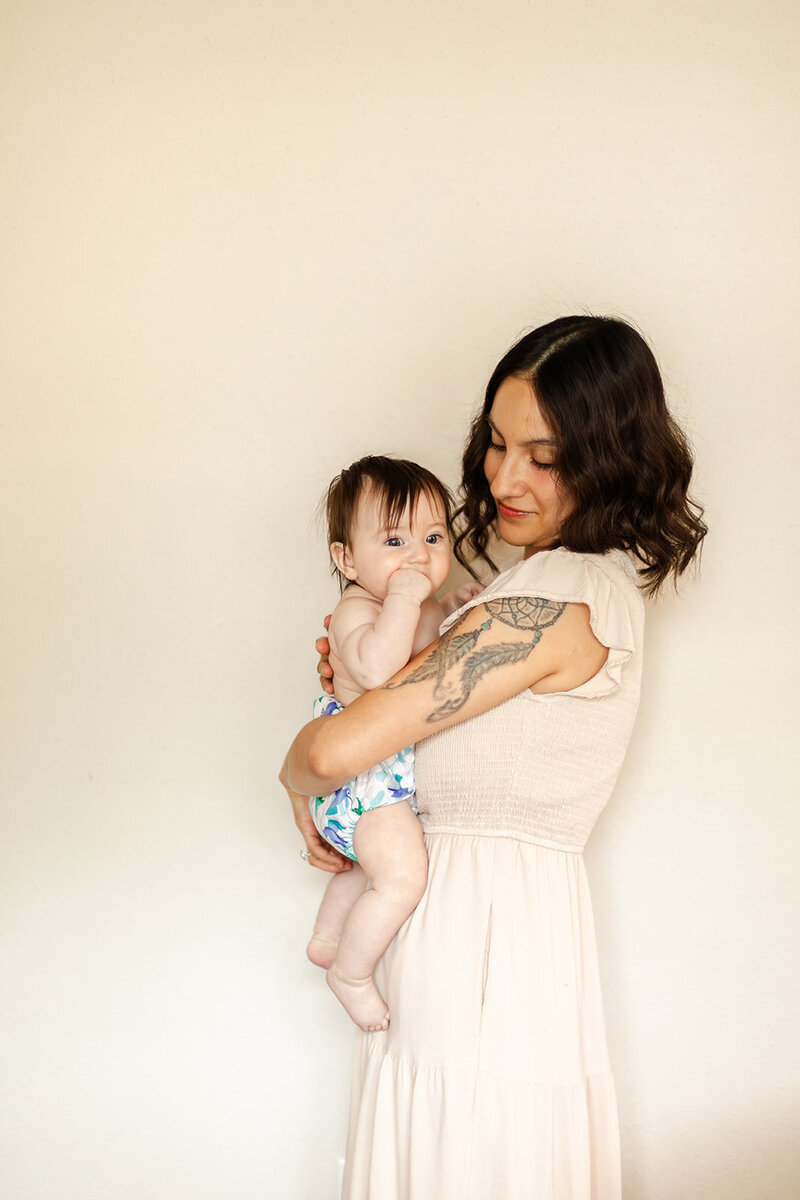 Milestone portrait taken in a neutral home in Pearland, Texaswith the mother in a creamy  dress while holding her baby wearing a cloth diaper