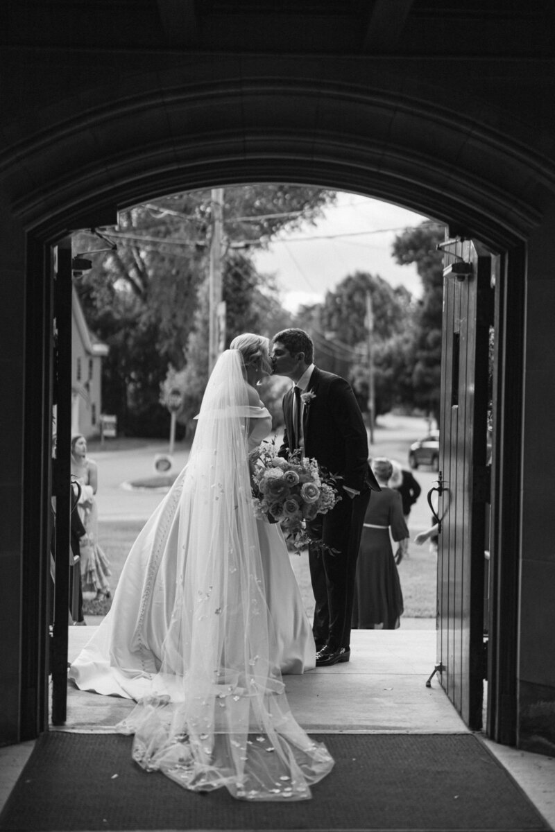 A groom leans the bride back for another kiss at the end of the wedding aisle.