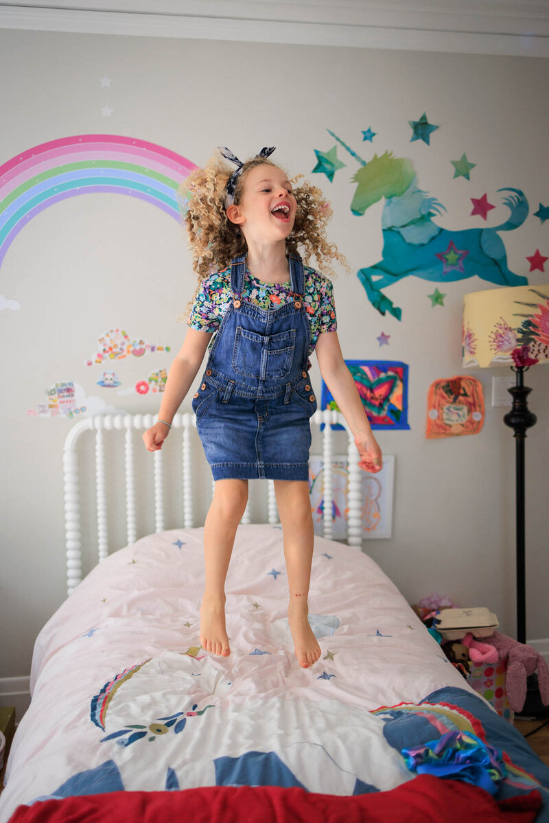 A 6-year-old girl jumping on her bed during an at home family photo session.