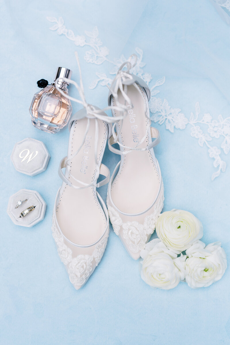 wedding shoes perfume and rings in flatlay with white ranunculus