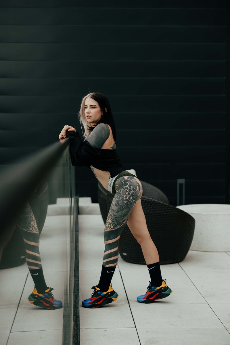Tattooed Woman Leaning Against Reflective Glass Wall