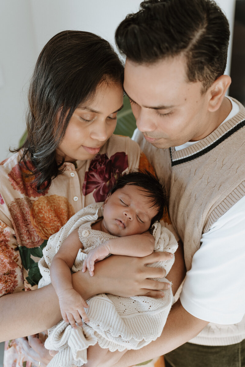 A Brisbane couple gently holds a sleeping baby wrapped in a knitted blanket.