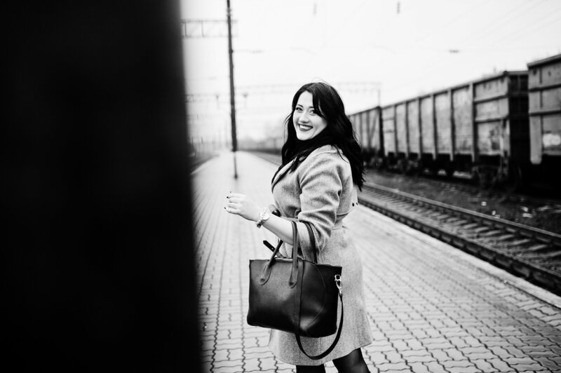 Girl holding large purse smiling over her shoulder at the camera while waiting for the train