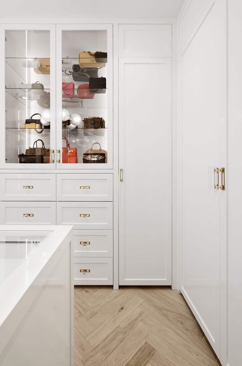 A white high gloss walk in closet with gold hardware accents. 