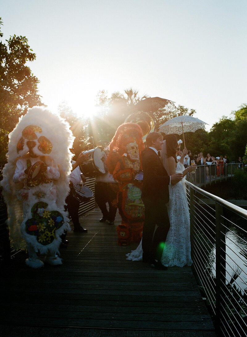 Second line over the bridge in new orleans wedding. Couple with umbrellas and mardi gras indians