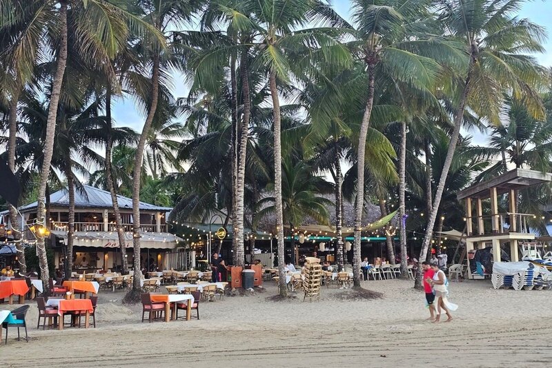 Rustic beach area with palm trees, shops, and families enjoying the coast in the Dominican Republic