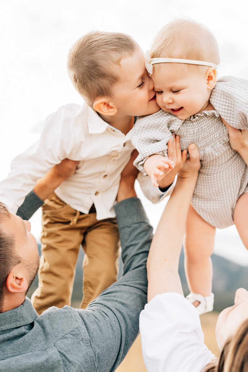 mom and dad lifting toddler boy and baby girl to the sky while brother kisses sister's cheek