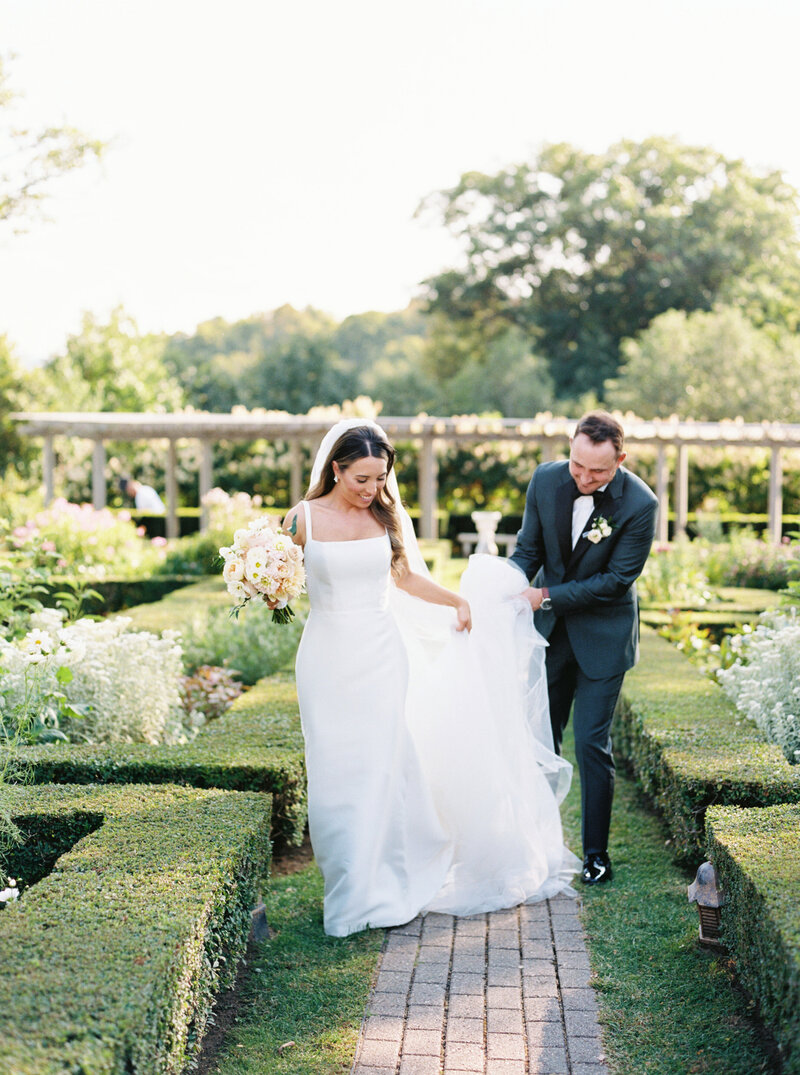 Groom helps bride with her dress in the Hildene, The Lincoln Family Home, gardens.