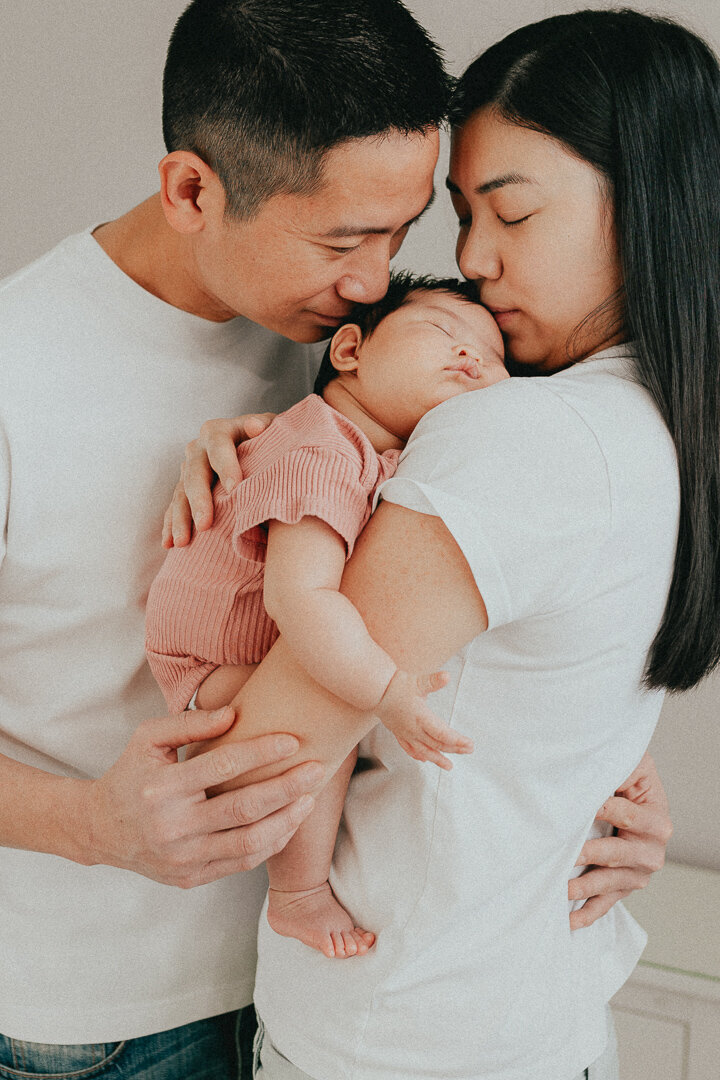 photo of a mom and dad snuggling their baby kissing her on the head taken in langley