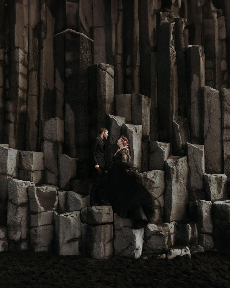 An elopement couple wearing all black standing on the basalt pillars at Reynisfjara black sand beach in Iceland.
