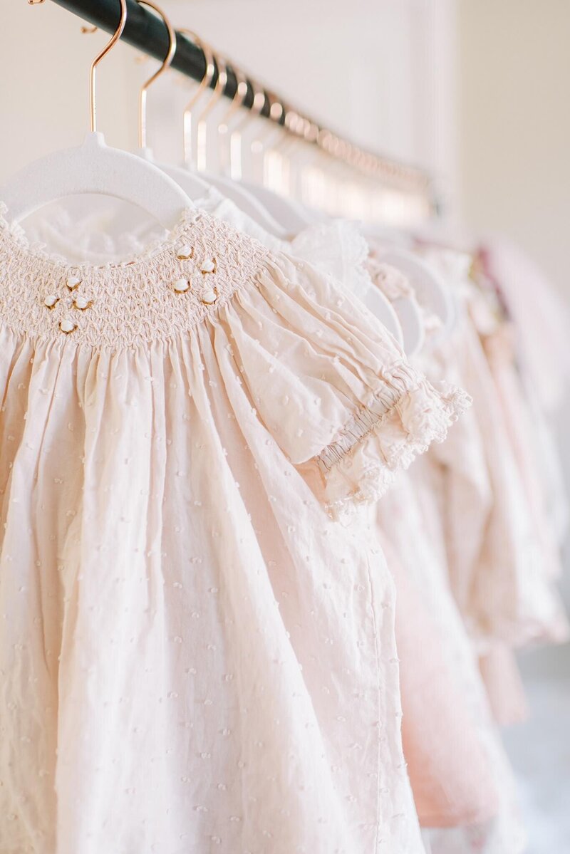 Dresses from Melissa Mayrie Photography's children's client closet hang on a rack displaying the soft tones and rich textures from a Noralee Maddie dress