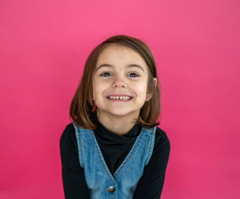 brunette girl smiling at the camera with a bubblegum pink backdrop