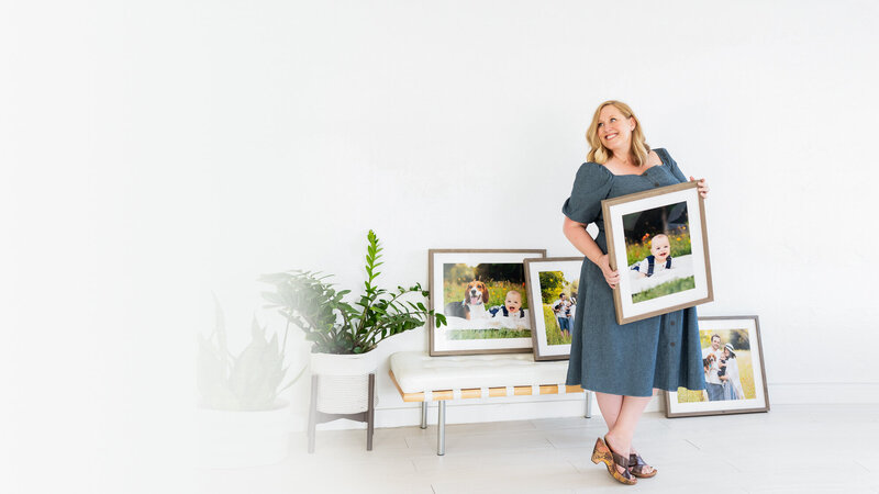 Best Boise Child and Family Photographer Tiffany Hix holding a framed portrait of a baby in her portrait studio in Boise, Idaho
