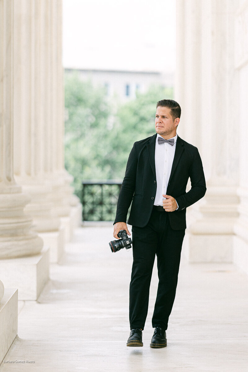 Luis Rivas, a DC Wedding Photographer, captured a timeless image of a man in a tuxedo and bow tie walking down a walkway in Washington DC.