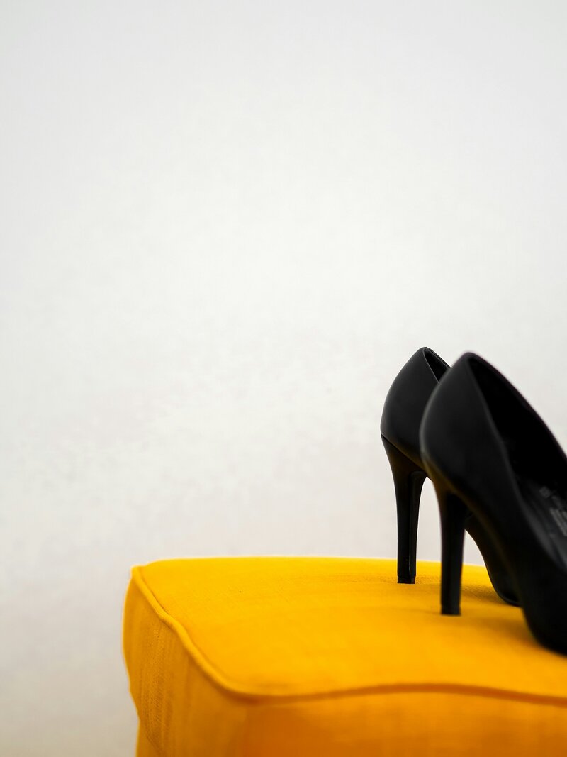 A pair of black heels sitting on top of a yellow cushion in front of a white wall