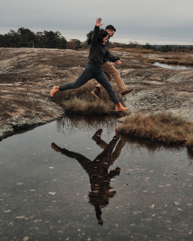 Couple jumps over a puddle with their reflection in frame