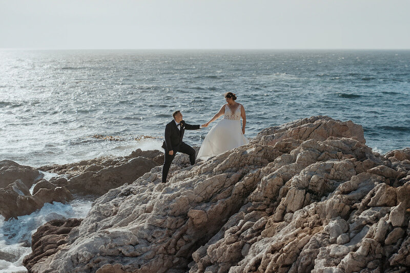 Bride leading groom up rocks with ocean in the background