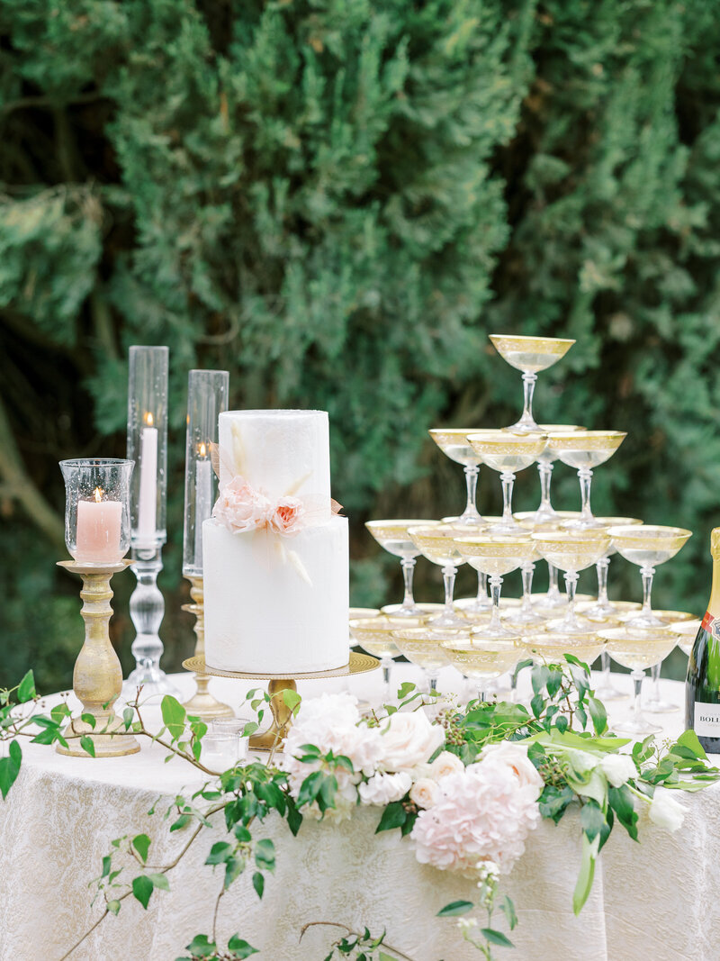 two tier cake with greenery, florals, candles, and champagne tower