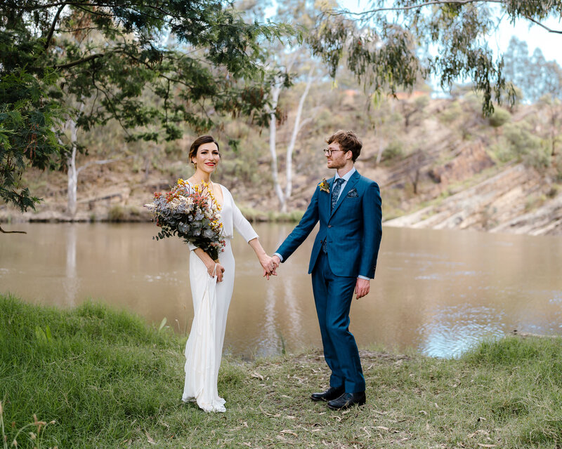 A newly wedded couple pose for wedding photos by a river