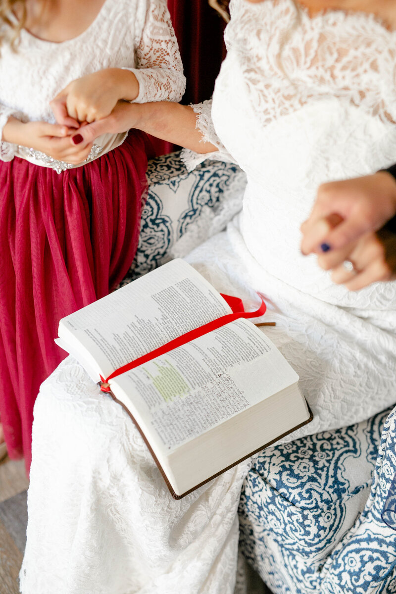 Open Bible  on lap of bride surrounded by women praying