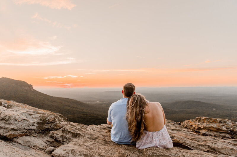Katie laying her head on her husbands shoulder while sitting on top of Hanging Rock, watching the sunset.