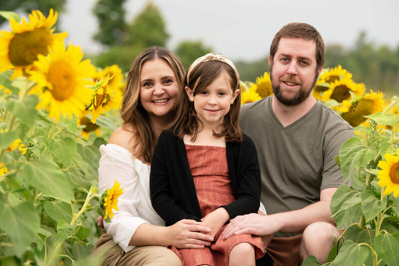 Mom and dad and daughter sitting down in a sunflower field for their family photos in Burlington.