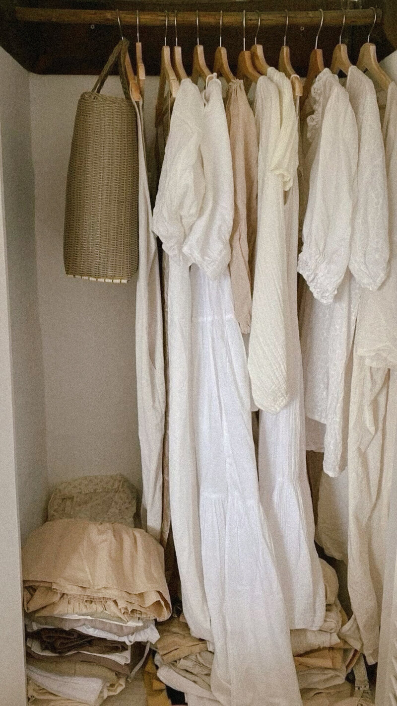 closet of womens loose fitting linen and cotten white and creamy colored clothes hung up and folded on bottom of the closet