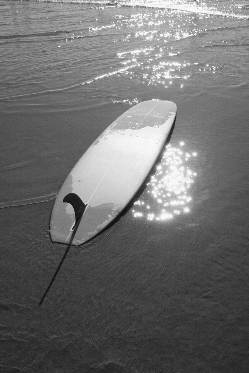 black and white photo of upside down surfboard on the sand