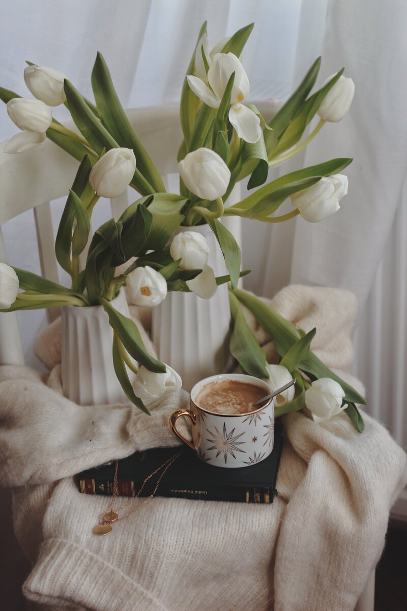 White flowers in vases next to a book and coffee
