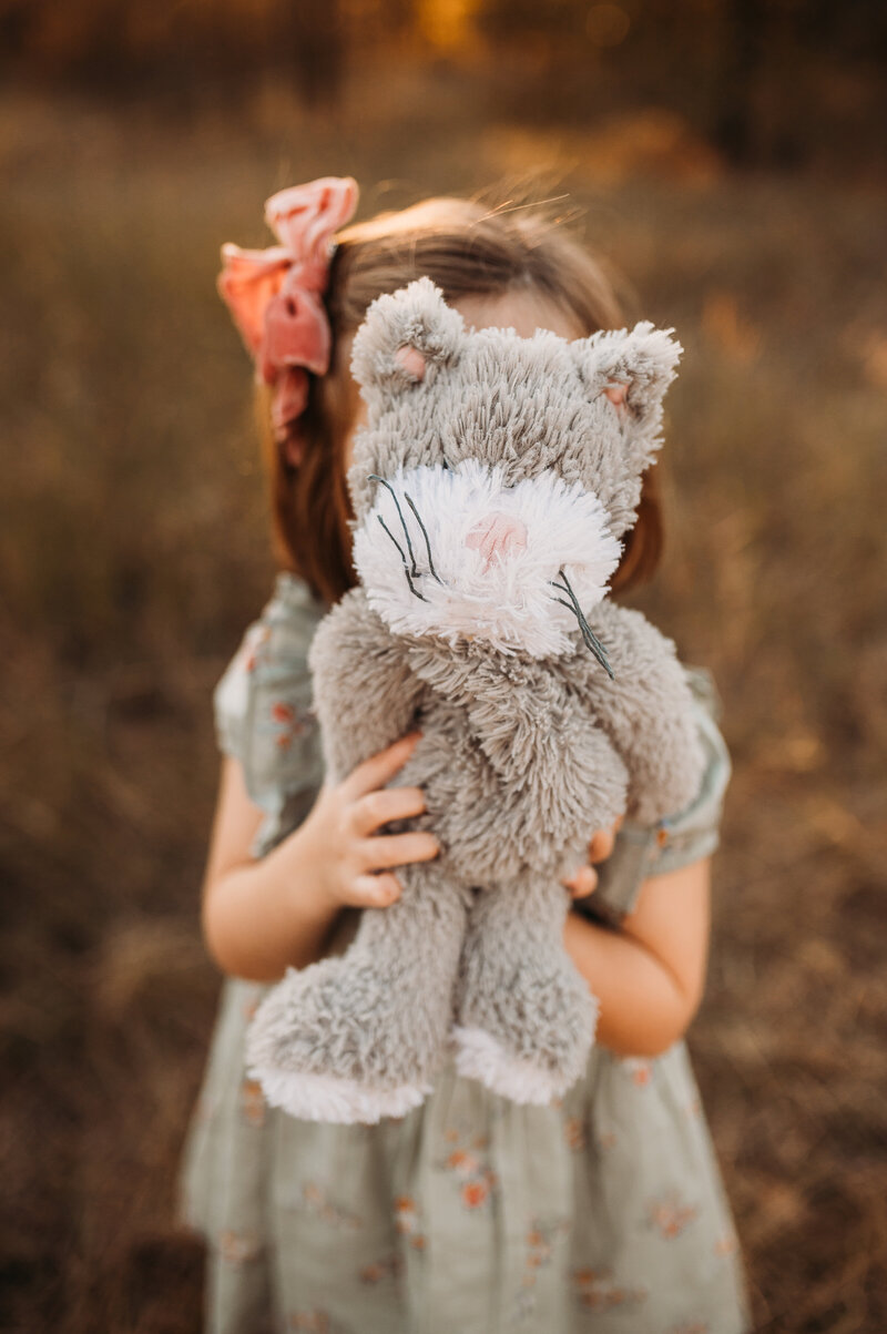 Toddler holding up her stuffed animal in front of her face.