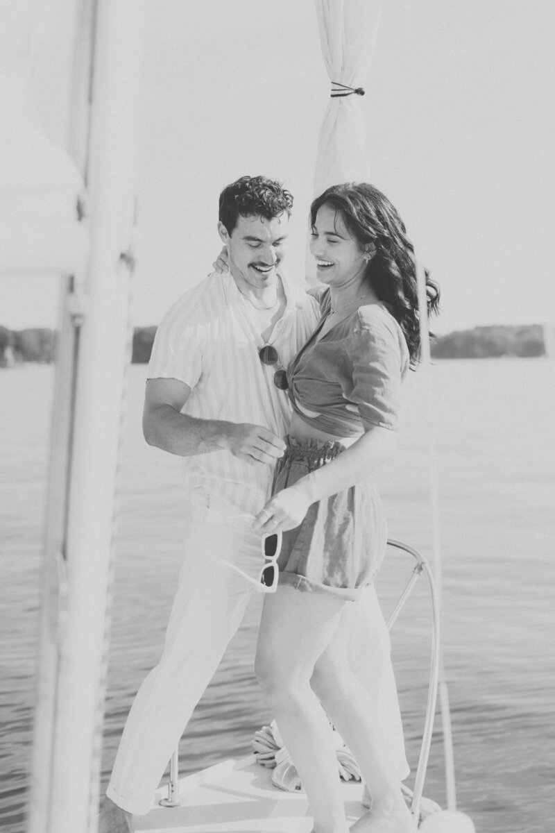 happy couple stand on sailboat holding sunglasses on charlotte lake