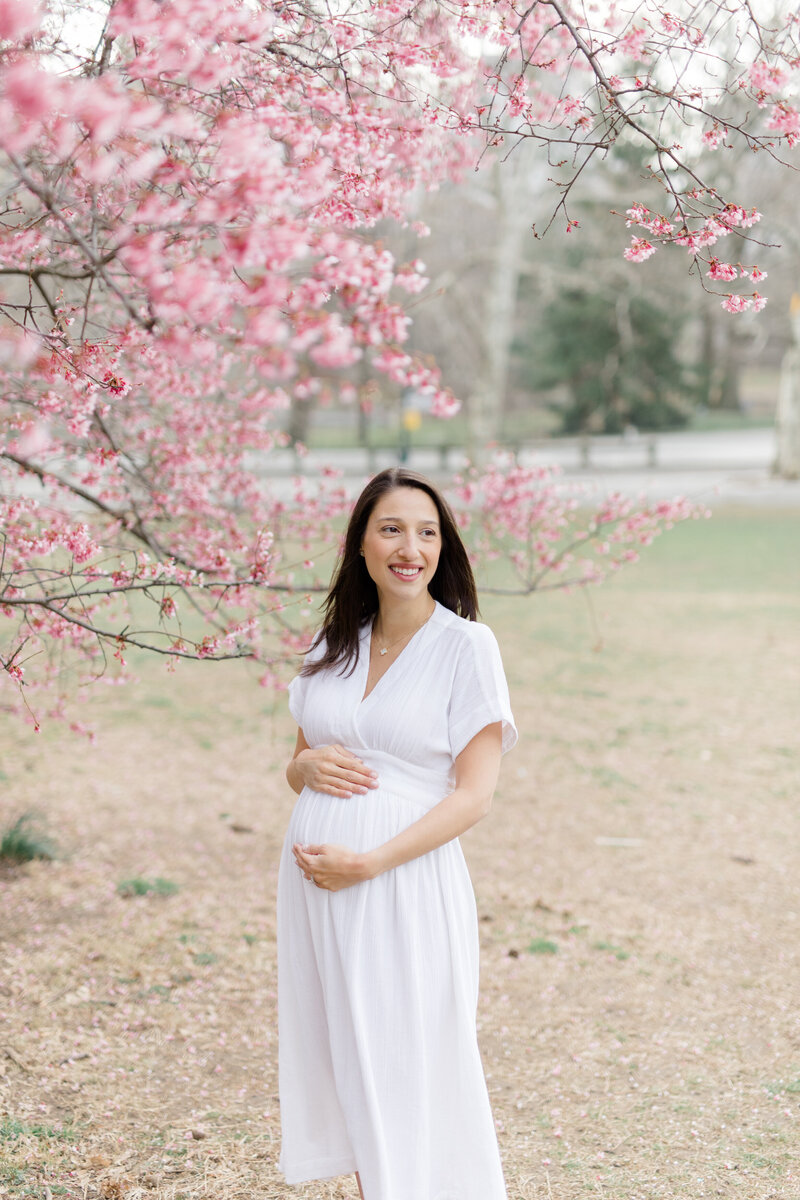 pregnant mom  in white dress in front of blooming tree by NYC maternity photographer