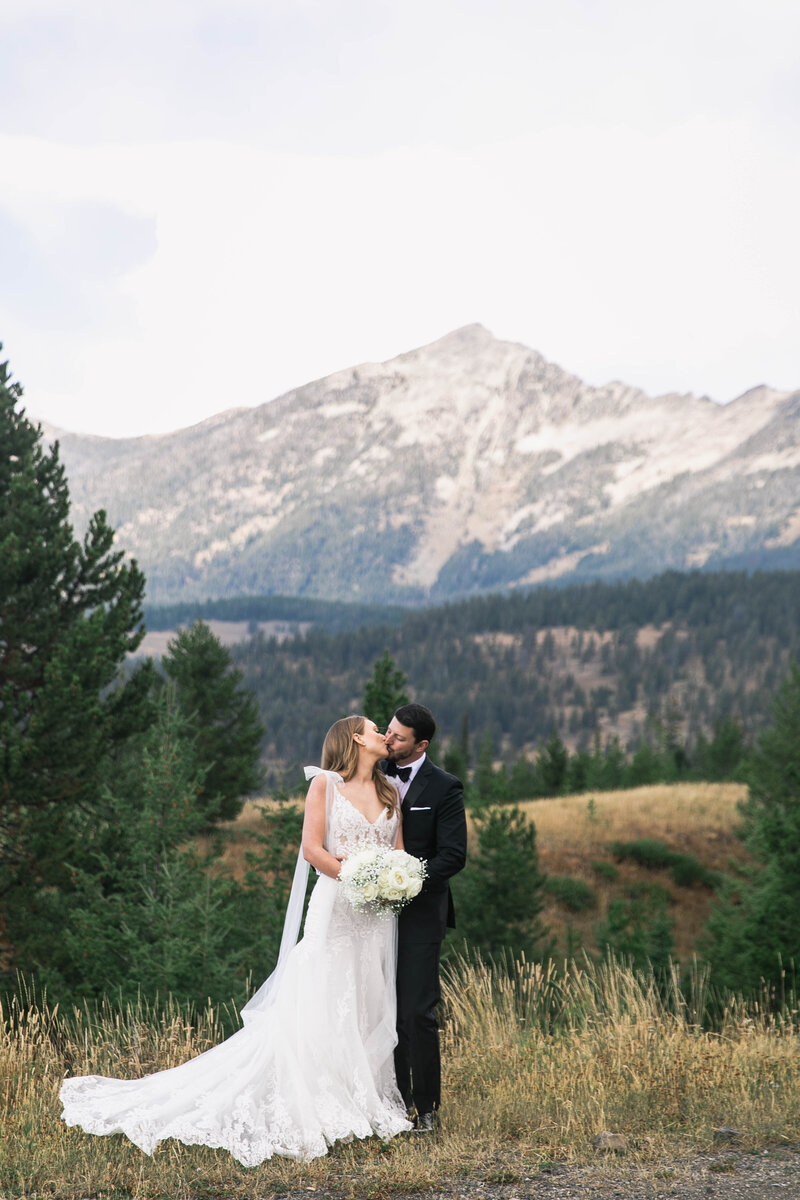 bride and groom kissing in front of mountains