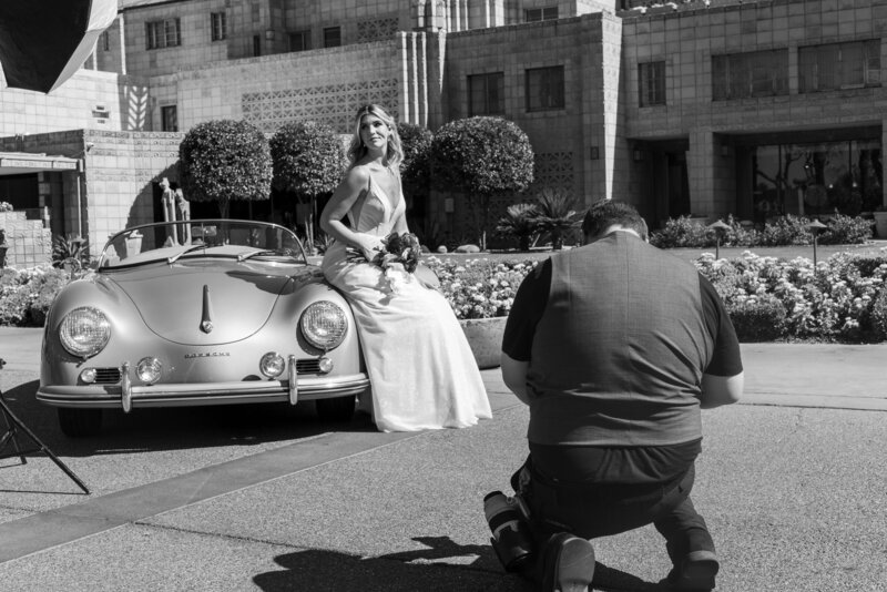 bride leaning on a car holding flowers