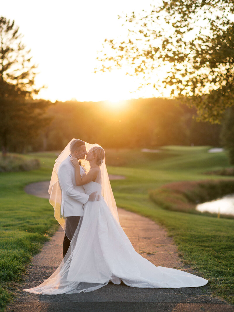 A groom in a white tux kisses his new wife during a sunset photo session after their Virginia Wedding