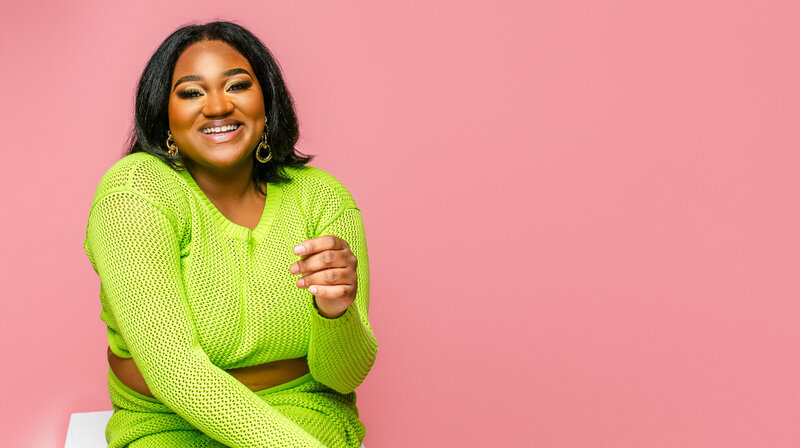 n this vibrant in-studio portrait, a plus-size pageant contestant shines in a stylish green knit coord set against a playful pink background, exuding confidence and grace.