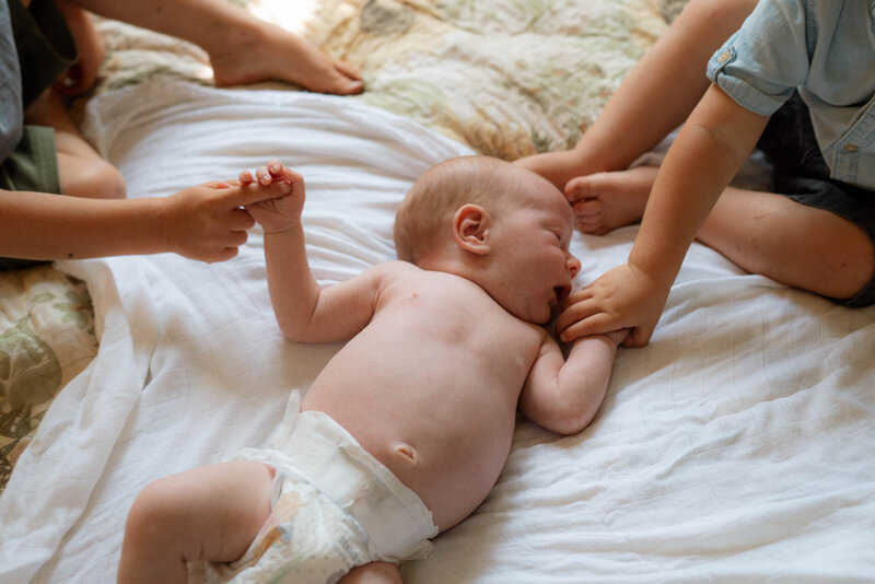 Brothers holding the hands of newborn baby brother