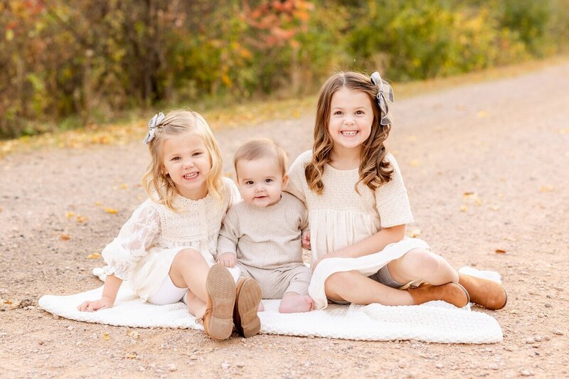 Three kids sitting on a blanket on a path to show family portraits minneapolis by Kacey Wyrick Photography