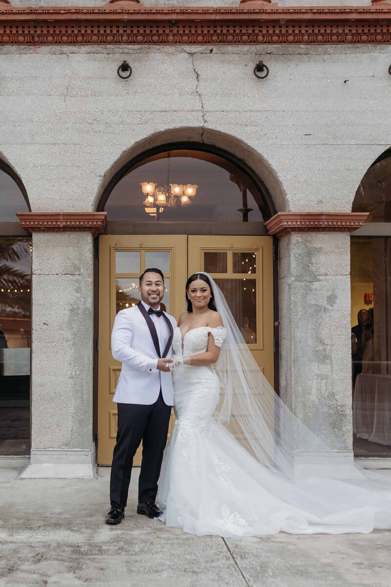 This elegant portrait outside a historic stone venue was captured by Phavy Photography, a Boston wedding photographer. The bride’s long train and the groom’s sharp white tux create a sophisticated look, while the editorial composition and candid joy reflect Phavy’s signature documentary style. Ideal for couples wanting timeless, high-end wedding photography in Boston and beyond.