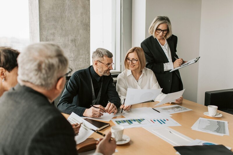 A group of older employees discuss data print-outs in a meeting