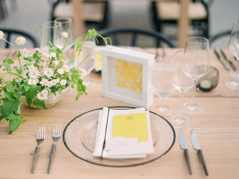 Table setting - a clear black rimmed plate with a napkin layered on it. Atop the napkin is a yellow menu