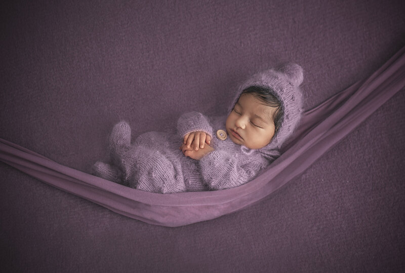 "Sleeping newborn gently resting in a soft fabric hammock, suspended in a serene pose, captured in a beautiful fine art photography session in Ottawa."